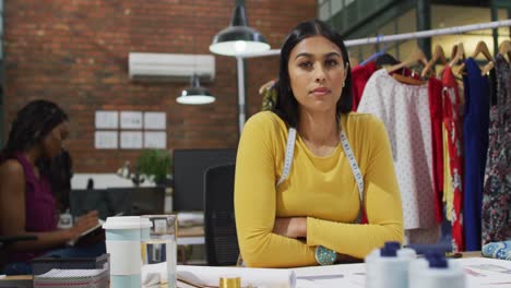 Portrait-of-happy-biracial-female-fashion-designer-wearing-tape-measure-at-office