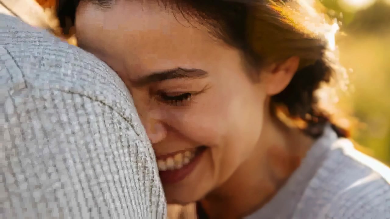 Mujer acurrucándose y apoyándose en el hombro de la chaqueta texturizada de su pareja al aire libre, con la luz dorada creando cercanía.