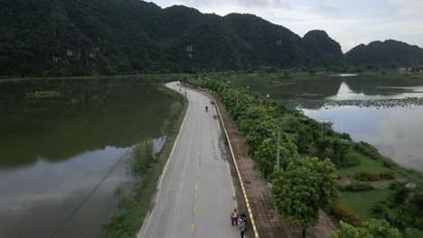 cool aerial shot following people on bikes on a asian road sounded my water and stunning green mountains in nin bihn, vietnam