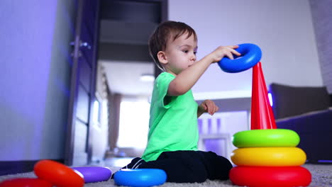 caucasian toddler boy sits on the floor in his room. cute child disassembles the toy pyramid. low angle view. low angle view.