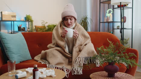 Sick ill woman suffering from cold or allergy sitting on home sofa sneezes wipes snot into napkin