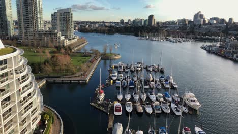 multiple pleasure yachts moored at scaffoldings at each sides of the false creek inlet in downtown vancouver between high buildings on a cloudy day