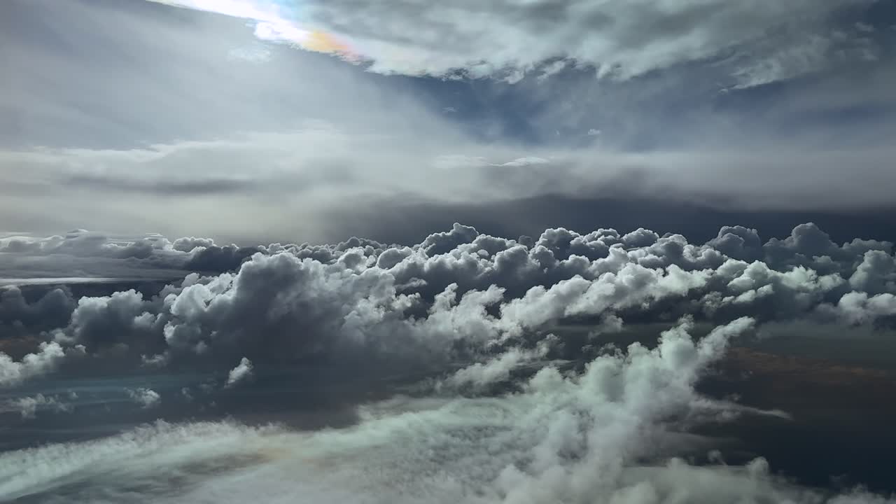 An aerial cloudscape through the eyes of the pilot while flying through dramatic darkening cumulus clouds, with a faded sun veiled by ethereal clouds