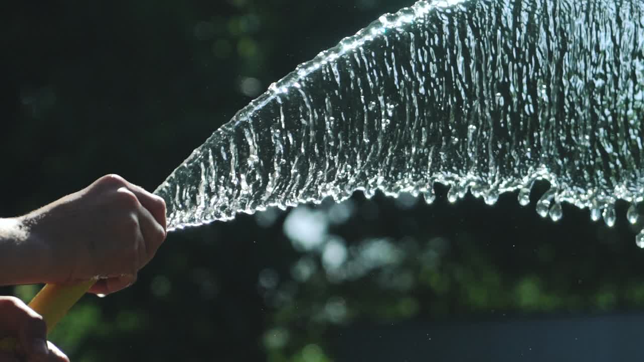 Stream of water spraying from garden hose, close up. Watering the green grass. Slow Motion.