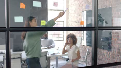 diverse male and female colleagues in discussion, brainstorming at glass wall in office, slow motion