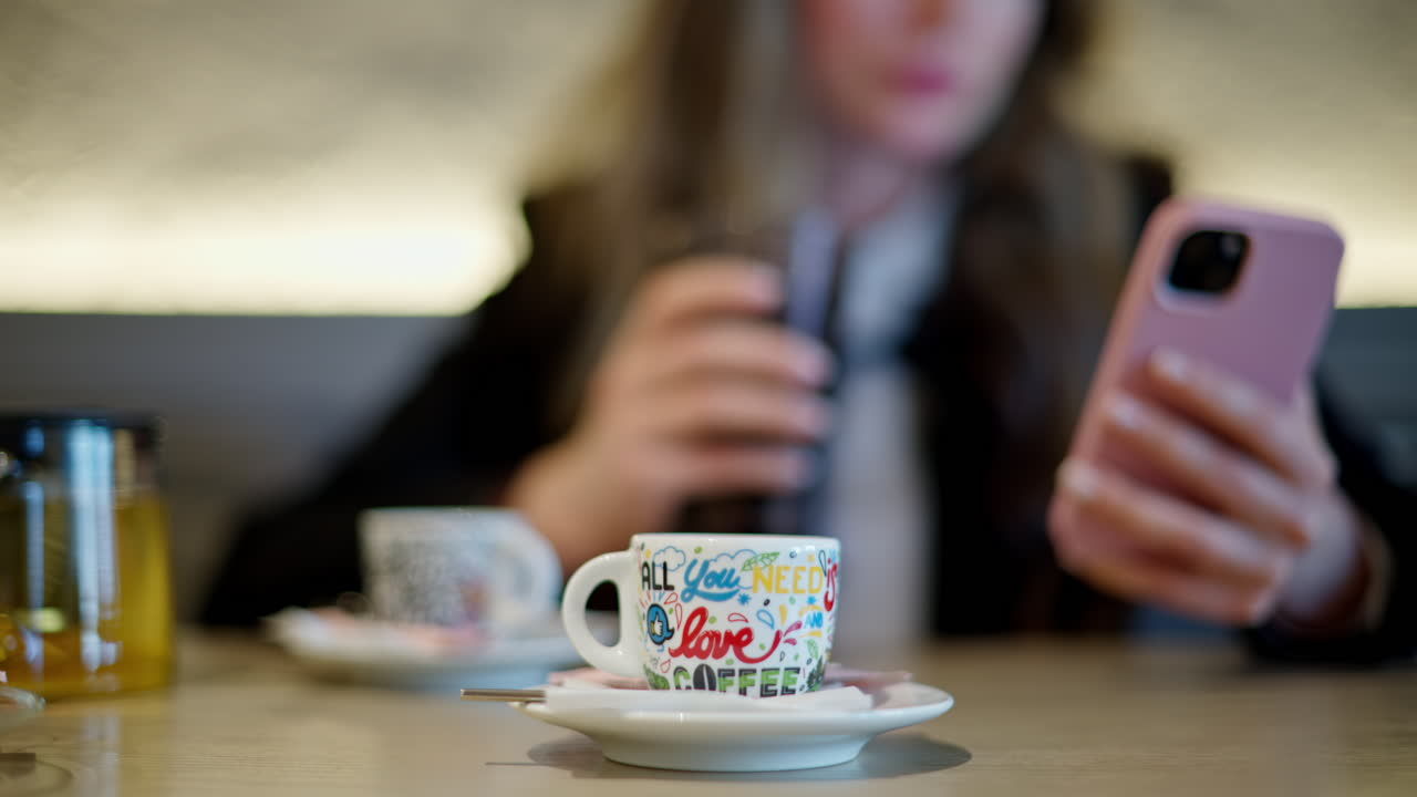 A cup of coffee at a cafe with a woman scrolling on her phone on the background
