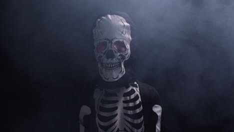 studio shot of child dressed up in skeleton costume trick or treating at halloween surrounded by smoke against black background