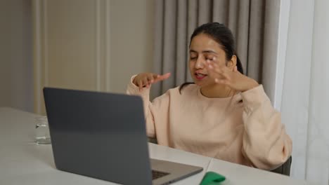 Happy-brunette-Indian-girl-in-a-beige-sweater-studies-foreign-languages-Italian-online-and-communicates-with-the-teacher-via-video-conference-on-gray-laptops-in-a-modern-apartment-during-the-day