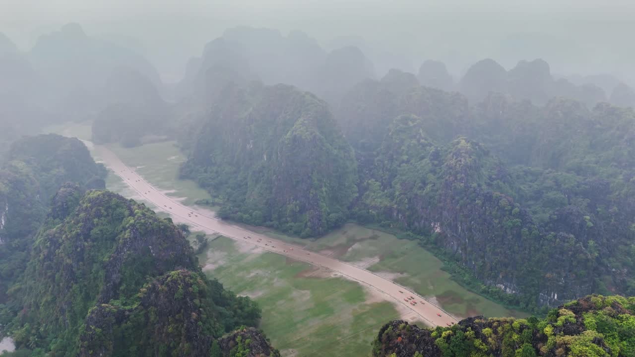 Misty aerial view over Hang Mua and Tam Coc in Ninh Binh, Vietnam, revealing limestone karst mountains, lush greenery, and a winding river cutting through the scenic valley landscape