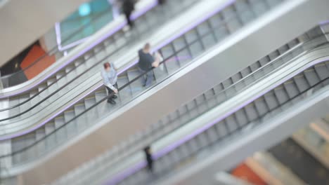 personas en movimiento en escaleras mecánicas en el centro comercial moderno. disparo con lente de cambio de inclinación con profundidad de campo súper superficial.