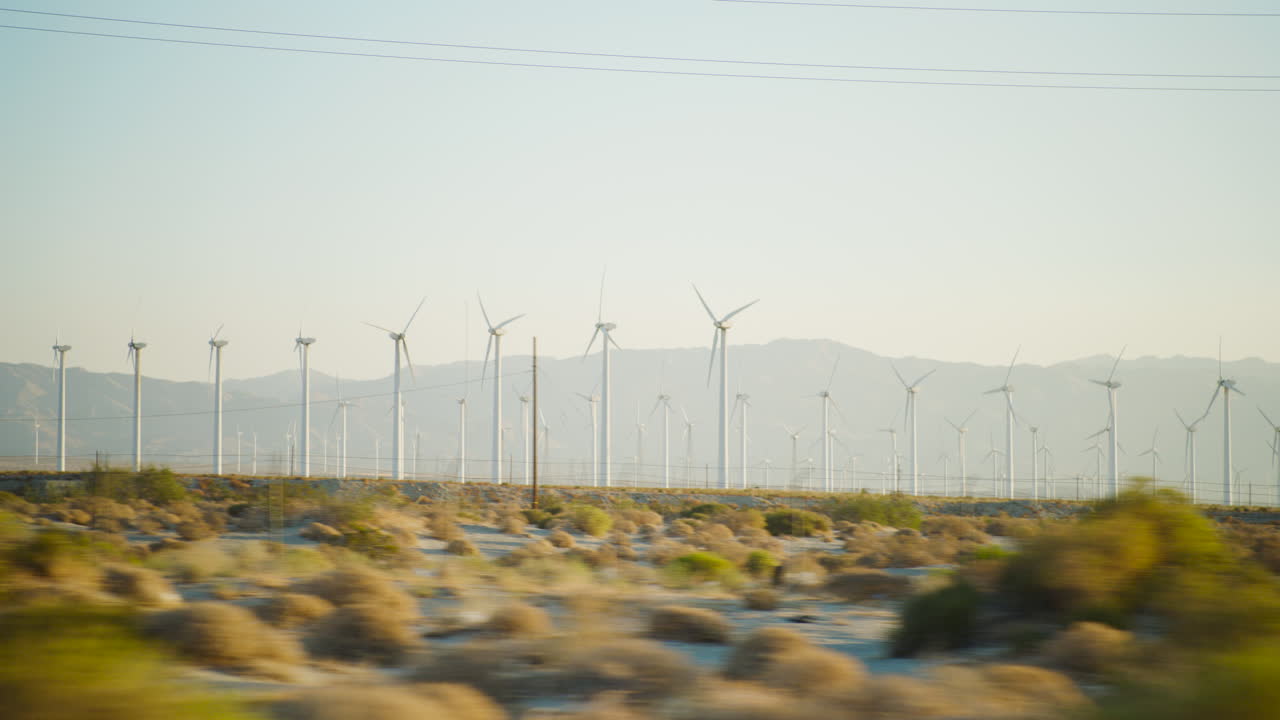 Palm Springs windmills in rows spinning at sunrise with the rugged San Jacinto Mountains rising behind them in California driving by point of view
