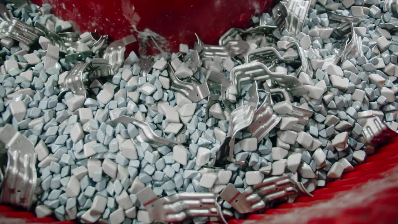 자동차의 금속 부품이 산업적으로 청소되고 진동하는 컨테이너에서 화학물질과 돌로 탈지름됩니다.