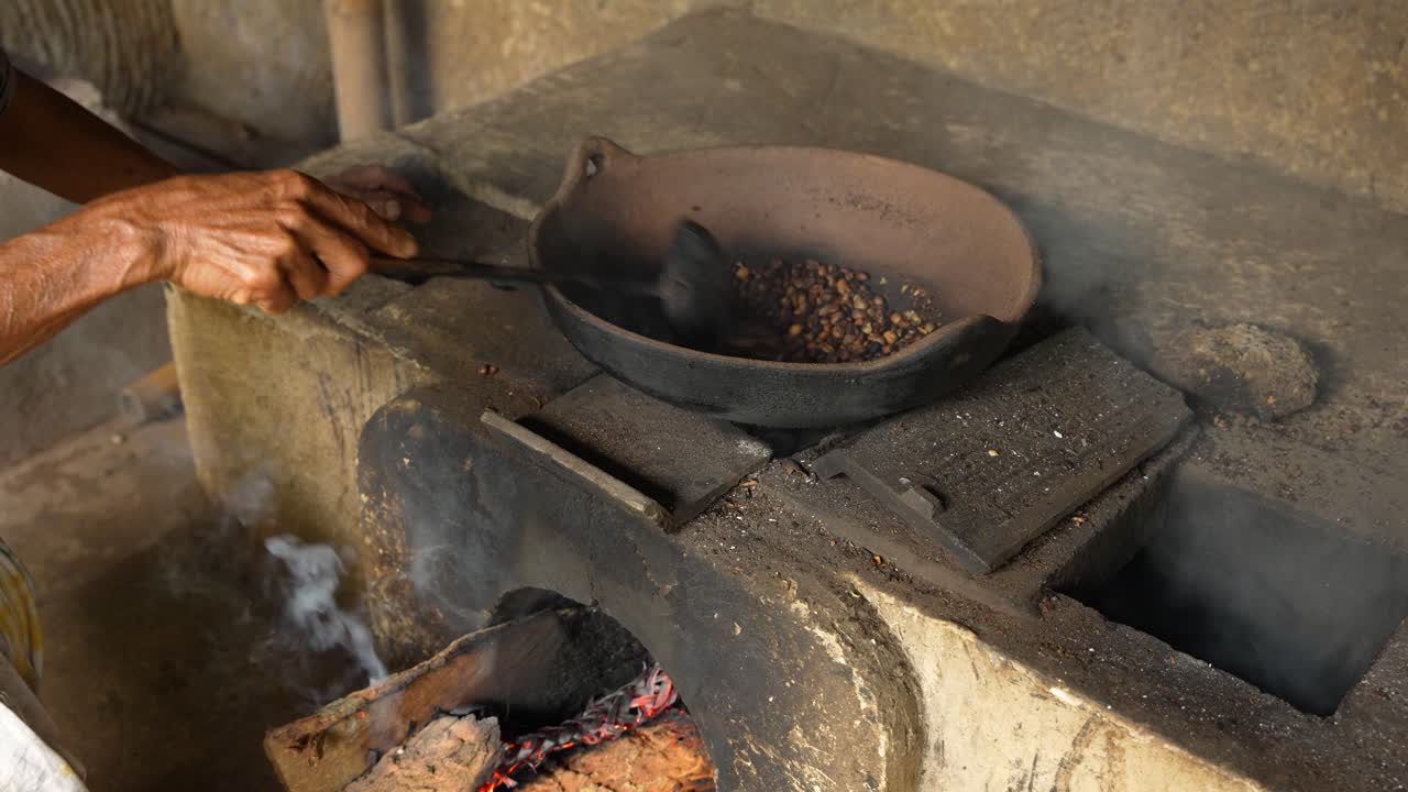 Coffee beans are hand-roasted in an iron pan over an open flame, showcasing authentic rural craftsmanship in a small village setting in Indonesia