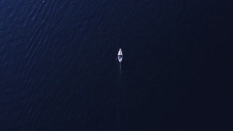 aerial top view of small boat slowly moving in deep dark purply blue sea