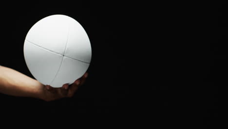 hand of african american man holding white rugby ball on black background, copy space, slow motion