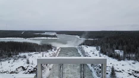 slow reveal drone shot snow covered road with rushing water notigi hydroelectric dam in the arctic