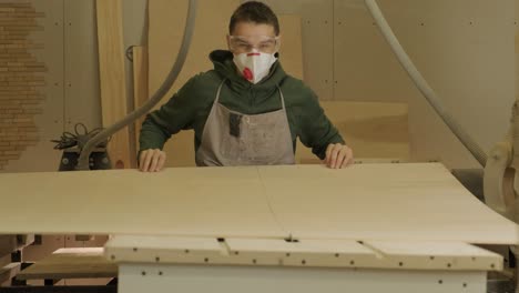 woodworker puts wooden plank, plywood panel, wood raw in the machine for cutting