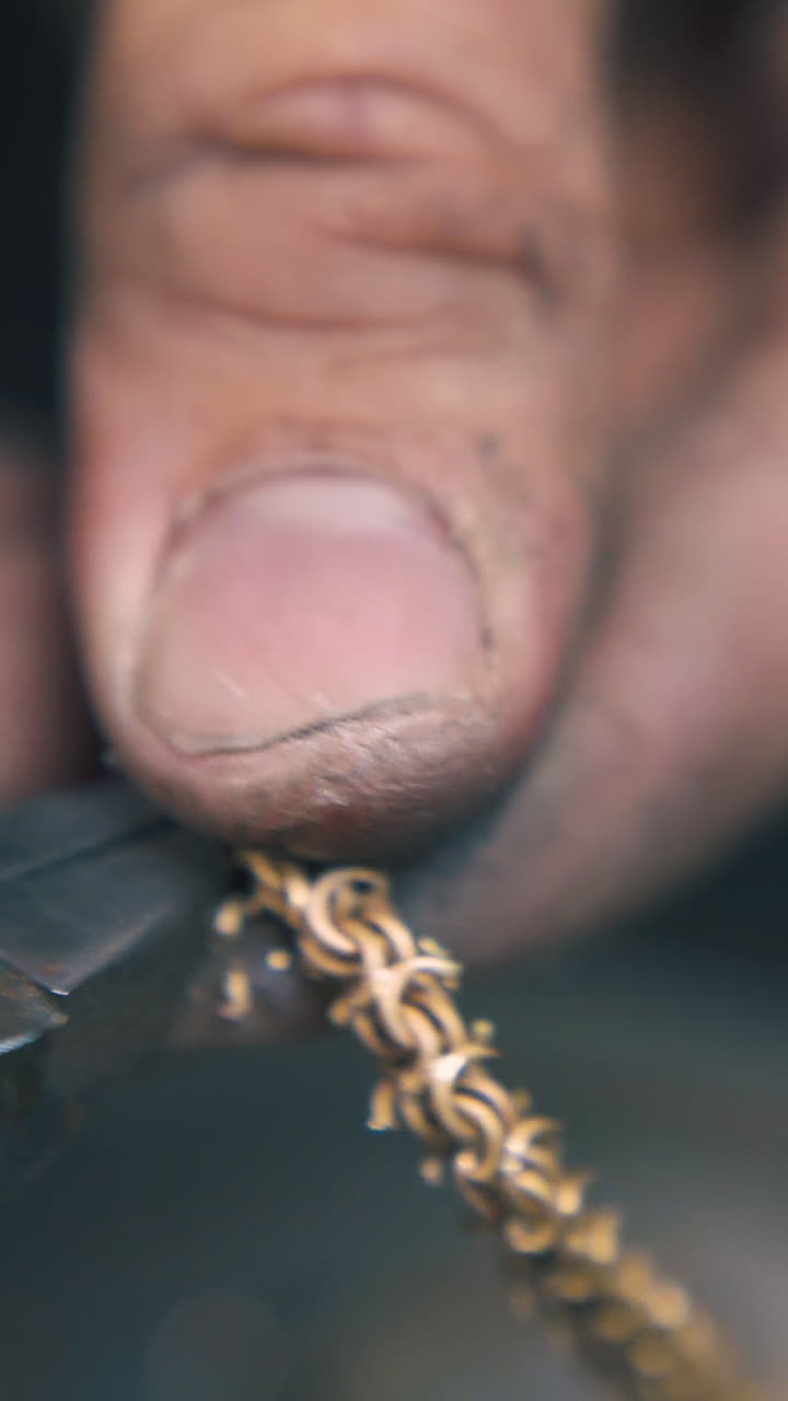 CU: goldsmith cuts leftover parts from shiny gold chain with old pliers on blurred background extreme close view