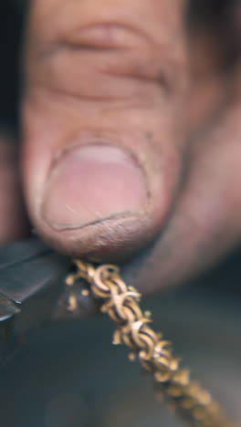 cu: goldsmith cuts leftover parts from shiny gold chain with old pliers on blurred background extreme close view