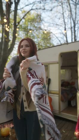 woman enjoying the fall in a cozy blanket near a travel trailer