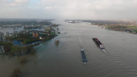 Vista-Aérea-Del-Histórico-Castillo-De-Slot-Loevestein-Rodeado-De-Aguas-Inundadas-Mientras-Dos-Barcos-Pasan-Por-El-Río-Waal-Cerca-De-Gorinchem,-Países-Bajos,-Después-De-Que-Las-Fuertes-Lluvias-Azotaran-El-Norte-De-Europa