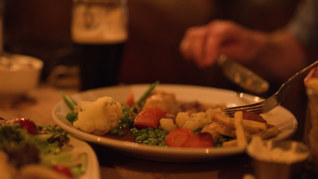 Diner cuts and eats steak pie with vegetables in warmly lit, rustic restaurant setting