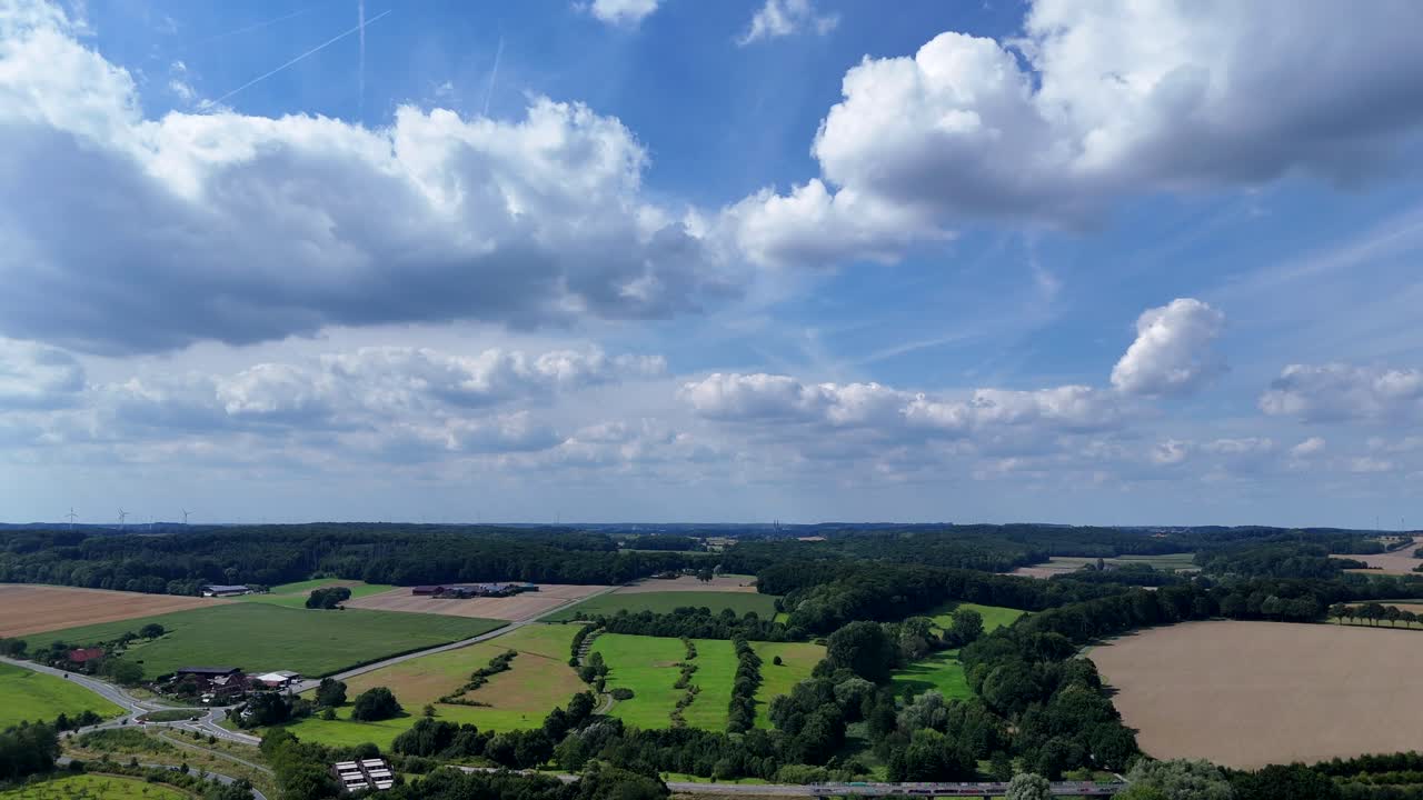 Aerial panorama shot of green forest landscape, rural fields and white clouds at blue sky. American neighborhood with idyllic lush scenery and highway. Wide shot. Serene atmosphere in u.s