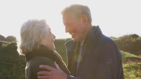 Amorosa-Pareja-De-Ancianos-Activos-Abrazándose-Mientras-Caminan-Por-El-Sendero-Costero-Contra-El-Sol-Abrasador