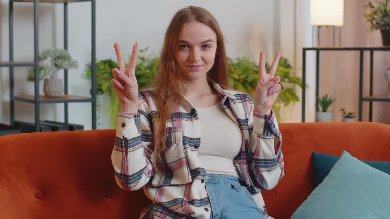 Young woman looking at camera showing victory v sign hoping for success win doing peace gesture