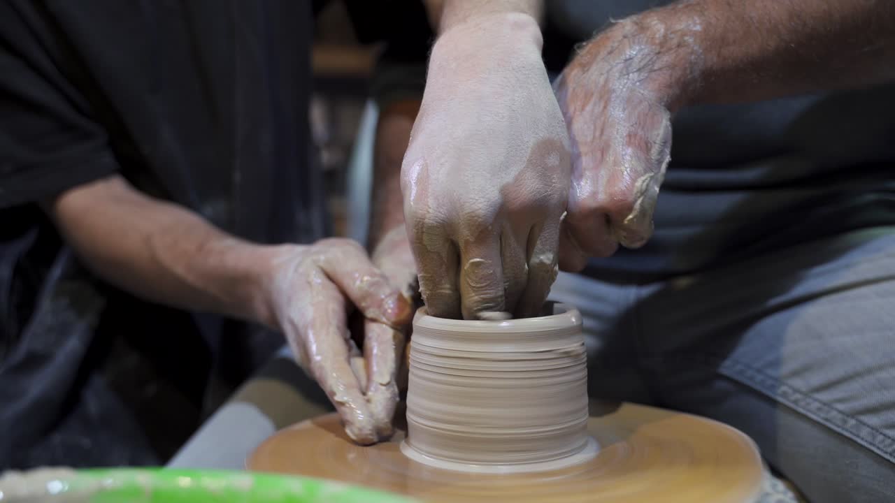 Two people shaping clay on a pottery wheel