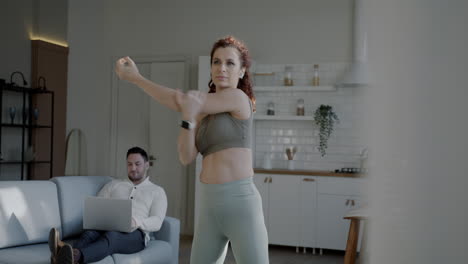 woman working out at home while partner uses laptop