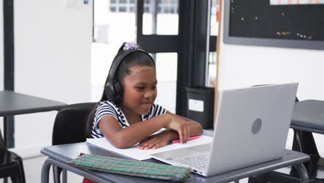 in a school classroom, a young african american girl is engaged with a laptop