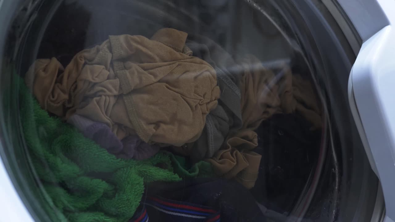 Clothes tumble within a washing machine during a spin cycle. A full load creates a dynamic, swirling motion