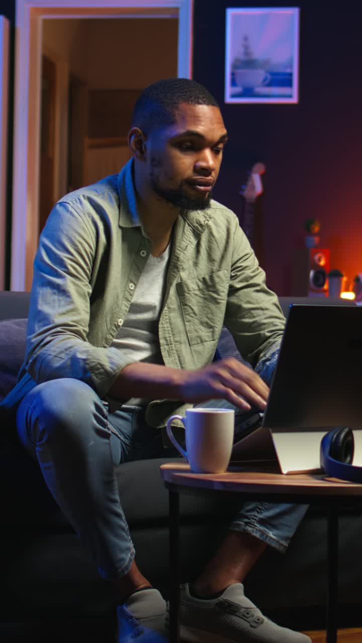 Vertical Video Young black guy working on his freelance tasks in the living room