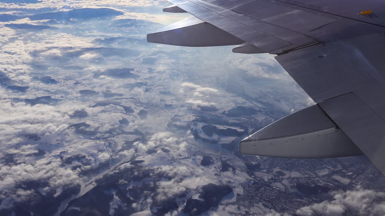 Udsigt fra flyvindue med vinge og motor over schweiziske bjerge og floder, med solbeskinnede skyer nedenunder