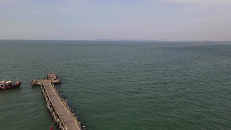 Aerial-footage-sliding-to-the-left-revealing-the-Pattaya-Fishing-Dock-and-a-fishing-boat-docked-with-a-Thai-flag,-Pattaya,-Thailand