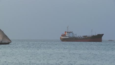 a dhow sailboat sails past a modern cargo ship off the coast of zanzibar