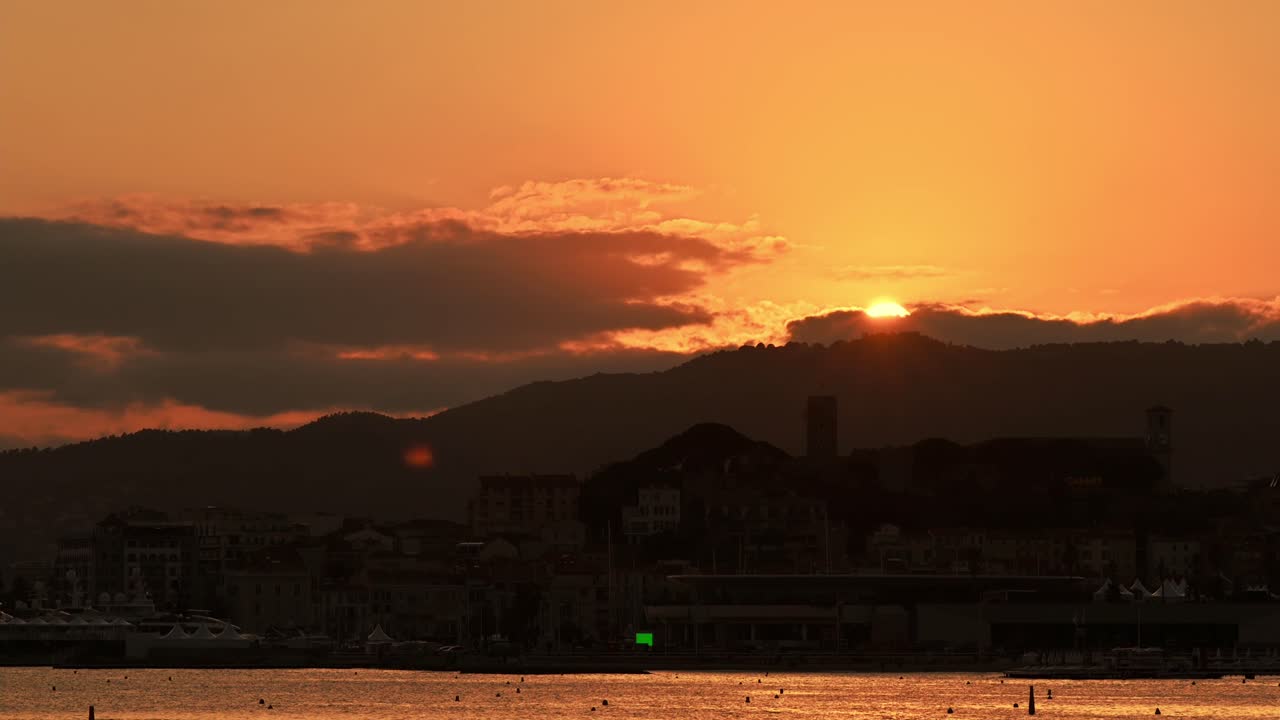 View of the Mediterranean sea coast in Cannes at sunset, France. Sun going behind the horizon, beach, buildings