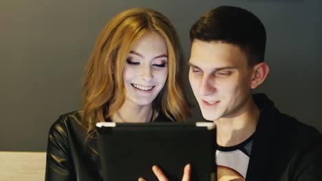 man and woman 20-25 years use the tablet in a cafe or office laughing and smiling