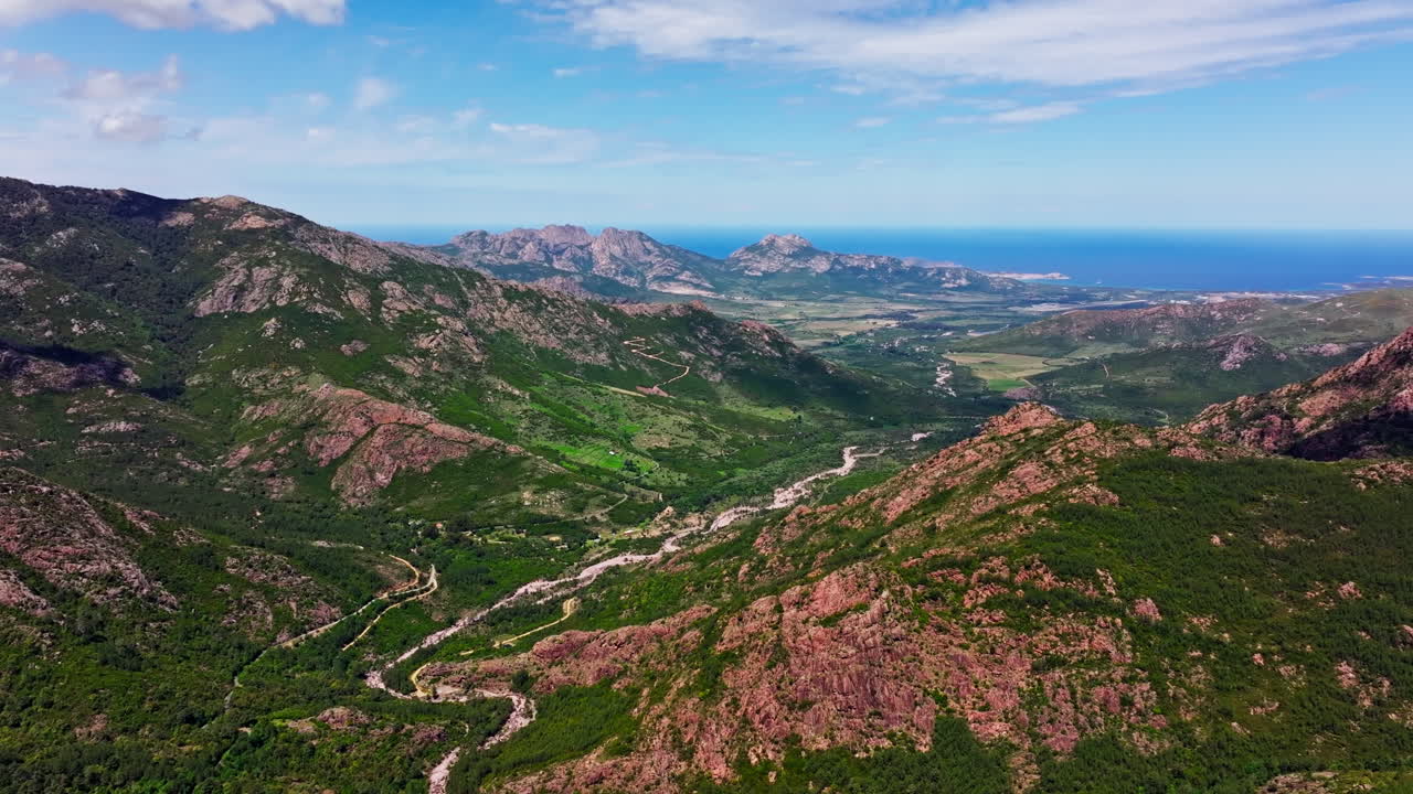 Aerial drone view over the mountainous landscape of Corsica. High view of green rugged landmark and the sea in the distance