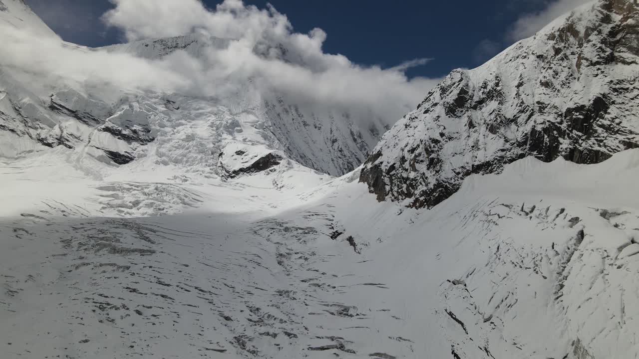 A breathtaking drone angle reveals glacier-carved terrain leading up to Mount Everest, surrounded by towering Himalayan formations. The high-altitude atmosphere highlights Nepal’s dramatic scenery