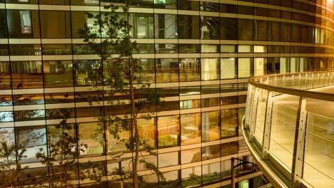 timelapse reveals a modern building at night with a curved glass facade reflecting the orange glow from the street lights and a balcony with glass railing