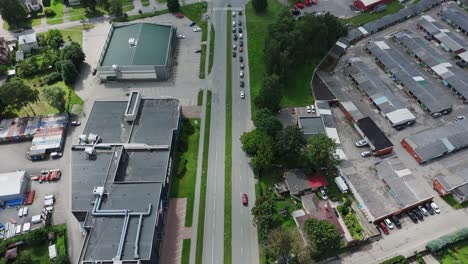 Aerial top-down view of Darzciems showing a main road flanked by industrial buildings, houses, and lush green trees on a sunny day
