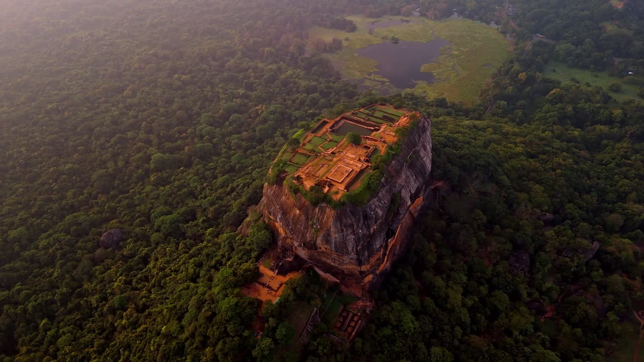 A stunning aerial clip of Sigiriya Rock at sunrise, surrounded by lush jungle and a serene lake reflecting the morning light.