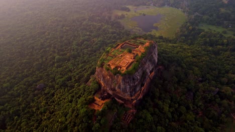 a stunning aerial clip of sigiriya rock at sunrise, surrounded by lush jungle and a serene lake reflecting the morning light.