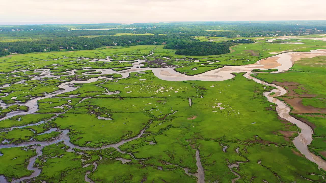 Drone video of Cape Cod marsh captures sandy inlets, reflective pools, and winding creeks cutting through lush grasses, offering a cinematic coastal perspective shaped by natural tides