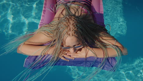 View-from-above:-A-child-with-afro-pigtails-swims-on-an-inflatable-mattress-in-the-pool.-4k-video