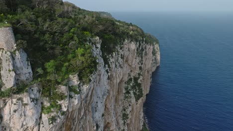 aerial shot of ancient ruins on capri's steep cliffs overlooking the blue sea