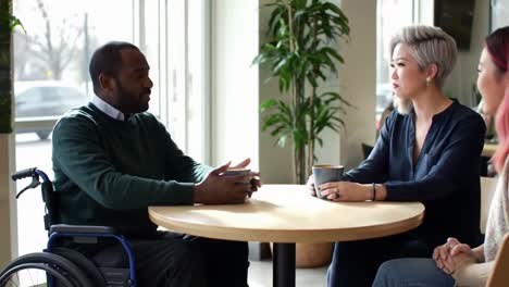 a man in a wheelchair and a woman enjoy a friendly conversation over coffee in a bright cafe,