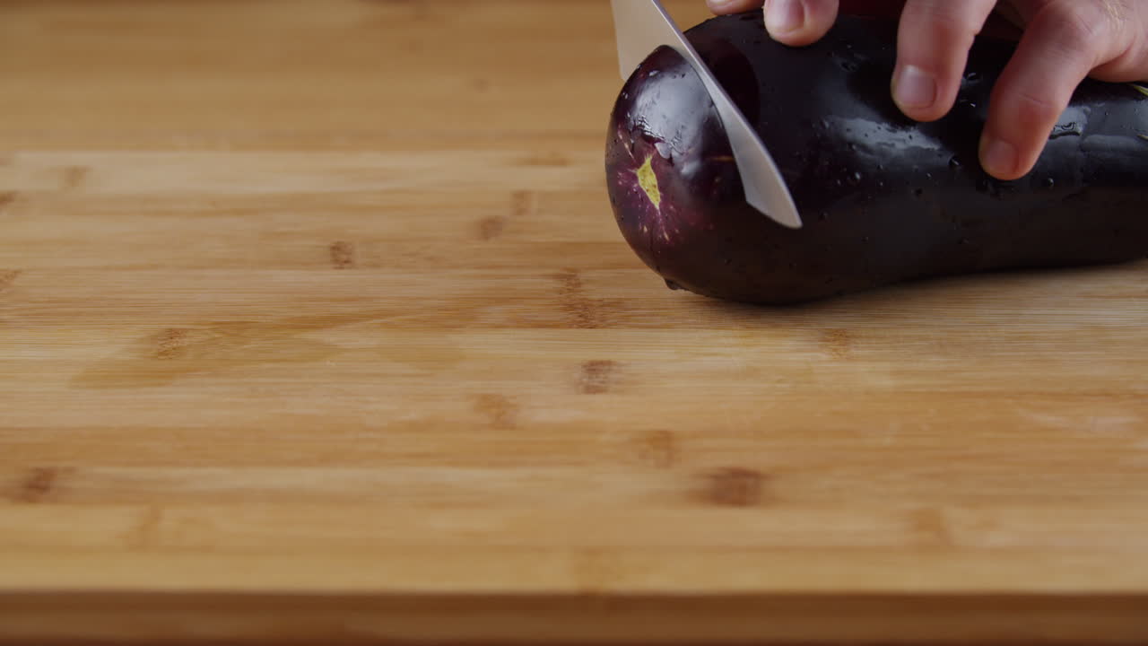 Skivar en bit kärnfri aubergine med en kniv i rostfritt stål - närbild
